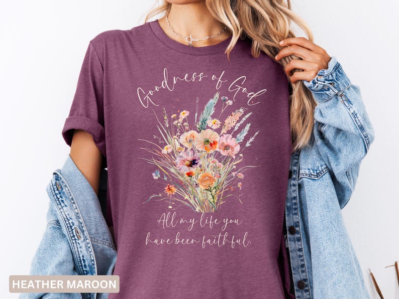 May include: Heather maroon t-shirt with a floral bouquet design. The shirt features the words "Goodness of God" and "All my life you have been faithful" in a script font. The floral arrangement includes pink, orange, and blue flowers.