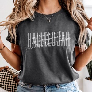 May include: A charcoal gray short-sleeve t-shirt featuring the word HALLELUJAH in large white block letters. Overlaid in white script is the text: So I throw up my hands and praise You again and again 'Cause all that I have is a Hallelujah.