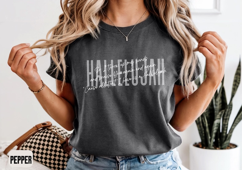 May include: A charcoal gray short-sleeve t-shirt featuring the word HALLELUJAH in large white block letters. Overlaid in white script is the text: So I throw up my hands and praise You again and again 'Cause all that I have is a Hallelujah.