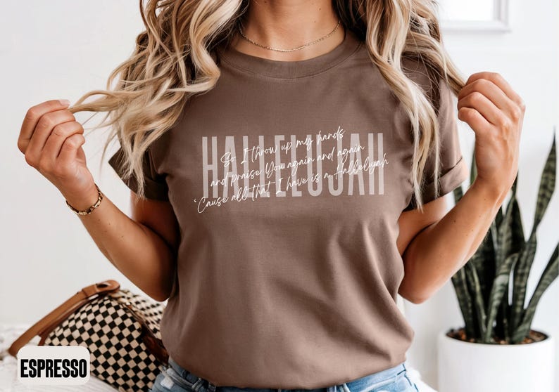May include: A brown short-sleeve t-shirt featuring the word HALLELUJAH in large white block letters, with the cursive text 'So I throw up my hands and praise You again and again 'Cause all that I have is a hallelujah' layered over it.
