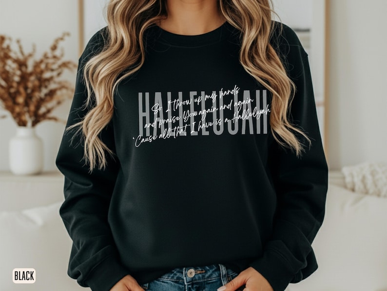 May include: A black long-sleeve crewneck sweatshirt featuring the word HALLELUJAH in large white block letters. Overlaid in a smaller white script font is the text: So I throw up my hands and praise You again and again 'Cause all that I have is a Hallelujah.