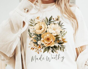 May include: White t-shirt with a floral design in shades of yellow and green. The text "Made Worthy" is printed below the flowers.
