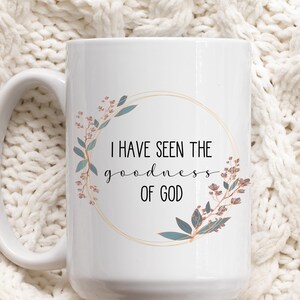 May include: White ceramic coffee mug with a gold circle and floral design. The text "I have seen the goodness of God" is printed on the mug.