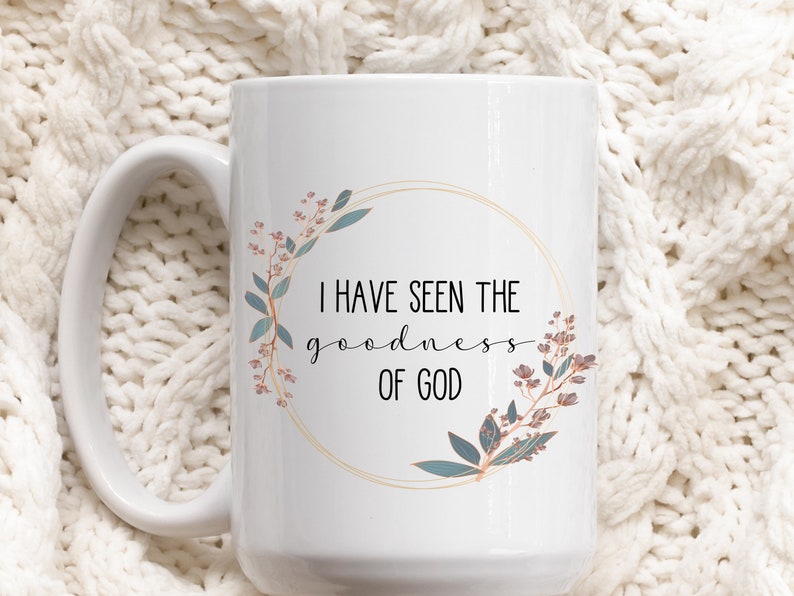May include: White ceramic coffee mug with a gold circle and floral design. The text "I have seen the goodness of God" is printed on the mug.