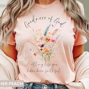 May include: Heather peach t-shirt with a floral bouquet design. The shirt features the script text "Goodness of God" above the flowers and "All my life you have been faithful" below. The shirt is a soft, comfortable material.