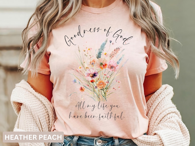 May include: Heather peach t-shirt with a floral bouquet design. The shirt features the script text "Goodness of God" above the flowers and "All my life you have been faithful" below. The shirt is a soft, comfortable material.