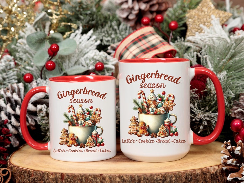 May include: Two white ceramic mugs with red interiors and handles. The mugs feature a "Gingerbread season" design with gingerbread cookies, candy canes, and text. The mugs are on a wooden surface with Christmas decorations.