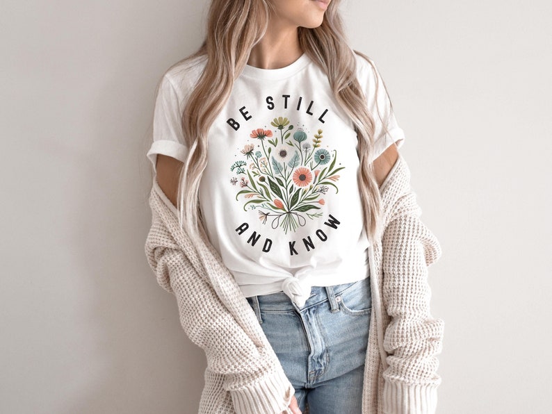 May include: White t-shirt with a floral design and the text "Be Still and Know" in black.