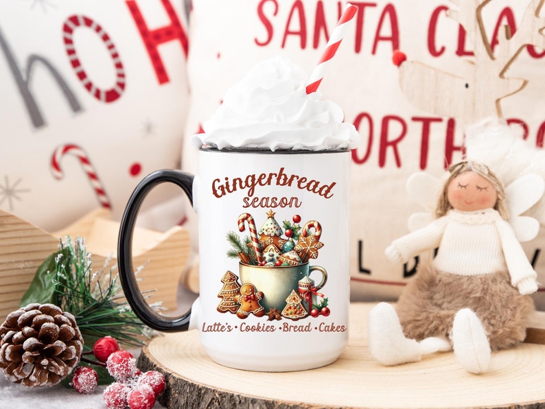 May include: White mug with a black handle, filled with whipped cream and a red and white striped straw. The mug features a "Gingerbread season" design with gingerbread cookies and text: Lattes, Cookies, Bread, Cakes. Christmas theme.