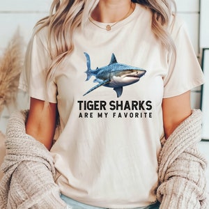 May include: A white t-shirt with a blue tiger shark graphic and the text "Tiger Sharks Are My Favorite".