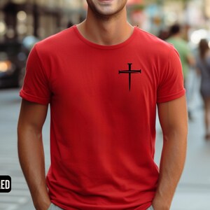 May include: A red t-shirt with a black cross design featuring nails. The cross is centered on the chest of the shirt.