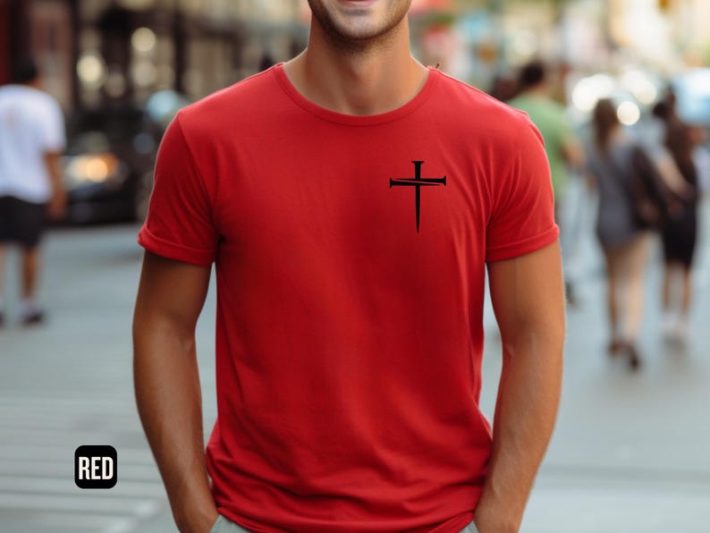 May include: A red t-shirt with a black cross design featuring nails. The cross is centered on the chest of the shirt.