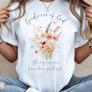 May include: White t-shirt featuring a watercolor floral design in shades of orange, pink, and green. The shirt has the text "Goodness of God" above the floral arrangement, and "All my life you have been faithful" below.