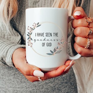 May include: White ceramic mug with a gold rim and floral design. The mug reads "I have seen the goodness of God".