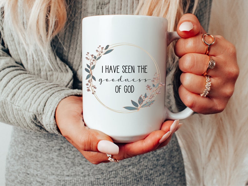 May include: White ceramic mug with a gold rim and floral design. The mug reads "I have seen the goodness of God".