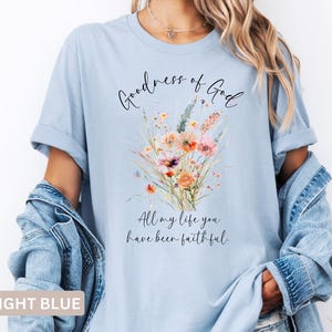 May include: Light blue t-shirt with the text "Goodness of God" and "All my life you have been faithful." A watercolor floral design in shades of orange, pink, and green is printed on the front.