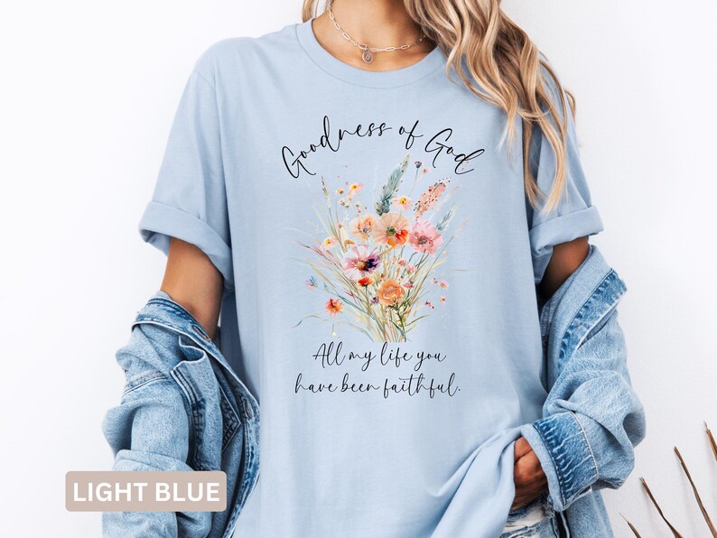 May include: Light blue t-shirt with the text "Goodness of God" and "All my life you have been faithful." A watercolor floral design in shades of orange, pink, and green is printed on the front.