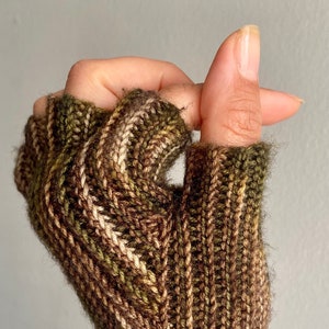 May include: A pair of fingerless gloves in a brown, green and cream striped pattern. The gloves are knitted and have a soft, fuzzy texture.