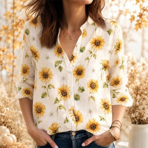 May include: A long-sleeved button-down shirt in an off-white color featuring a repeating pattern of yellow sunflowers with green stems and leaves. The shirt has a classic collar, a front button placket, and long sleeves with buttoned cuffs.
