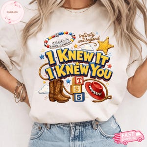 May include: A cream-colored t-shirt featuring a graphic print with the text "I KNEW IT I KNEW YOU" in blue and yellow, a beaded bracelet with "YOU'RE A GOOD COWBOY", a brown cowboy boot, a red hat, a lasso, alphabet blocks, and a gold star.