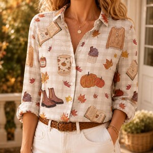 May include: A long-sleeve button-down shirt with a light beige and white gingham pattern. The shirt features a repeating print of autumn-themed illustrations including pumpkins, open books, brown boots, sweaters, cupcakes, and orange maple leaves.