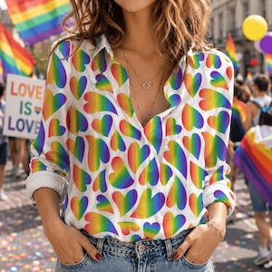May include: White button-down shirt with a rainbow heart pattern. The shirt features long sleeves and a collared neckline. The image includes the text "LOVE IS LOVE" on a sign in the background, along with rainbow flags and balloons.