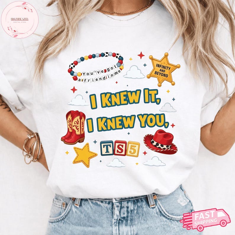 May include: A white t-shirt featuring a graphic print with the text I KNEW IT, I KNEW YOU, TS5, INFINITY AND BEYOND, and YOU'VE GOT A FRIEND IN ME. The design includes a beaded bracelet, a sheriff star, red cowboy boots, a red hat, and blocks.