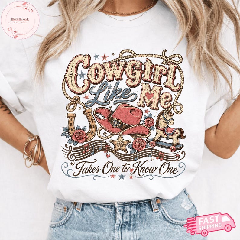 Op de afbeelding: Een wit t-shirt met een grafische print met de tekst Cowgirl Like Me en Takes One to Know One. Het ontwerp bevat een rode cowboyhoed, een hoefijzer, een hobbelpaard, een sheriffster, muzieknoten en touwelementen in rood en blauw.