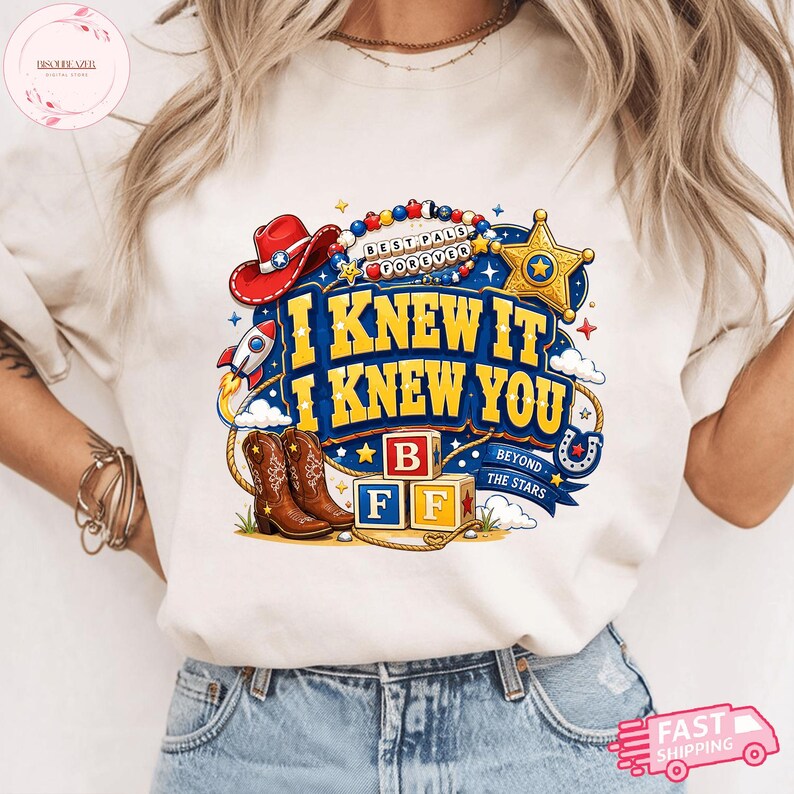 May include: A cream-colored t-shirt featuring a graphic print with the text I KNEW IT I KNEW YOU, BEST PALS FOREVER, and BEYOND THE STARS. The design includes a red cowboy hat, a gold sheriff star, a rocket, brown cowboy boots, and alphabet blocks.