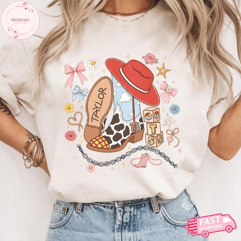 May include: A cream-colored t-shirt featuring a graphic print of a cow-print cowboy boot, a red cowboy hat, building blocks with the letters T, S, and the number 13, pink bows, flowers, and a beaded necklace with the text THE NEW YOU.