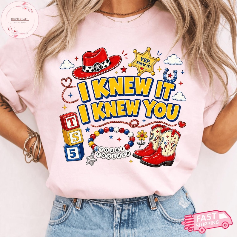 Pode incluir: Uma t-shirt rosa claro com uma estampa gr&aacute;fica com o texto I KNEW IT I KNEW YOU. O design inclui um chap&eacute;u de cowboy vermelho, uma estrela de xerife amarela, blocos coloridos, uma pulseira de contas com o texto YOU & I FOREVER e botas vermelhas.