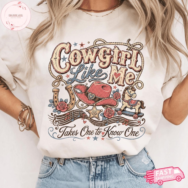Op de afbeelding: Een cr&egrave;mekleurig t-shirt met een grafische print met de tekst Cowgirl Like Me en Takes One to Know One. Het ontwerp bevat een roze cowboyhoed, een hoefijzer, een hobbelpaard, een sheriffster, rozen, muzieknoten en een lasso.