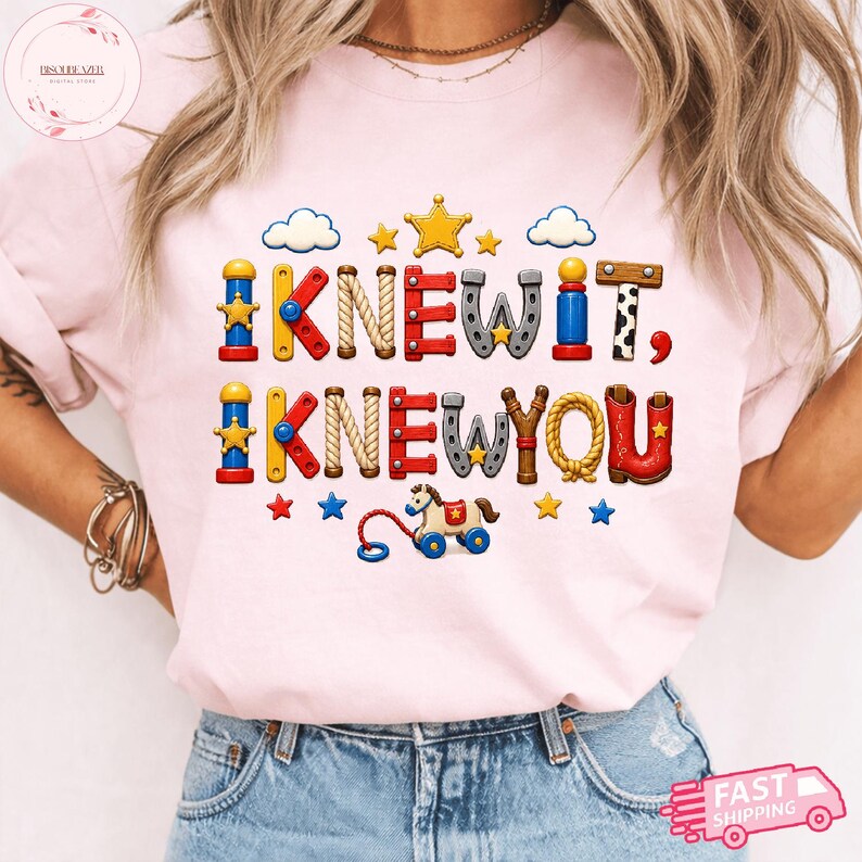 Puede incluir: Una camiseta rosa claro con un dise&ntilde;o gr&aacute;fico que incluye el texto I KNEW IT, I KNEW YOU. Las letras est&aacute;n estilizadas como varios juguetes, incluyendo bloques de construcci&oacute;n, cuerdas y una herradura, junto a estrellas, nubes y un caballo de juguete.