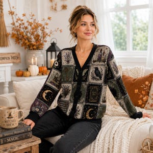 May include: A long-sleeve button-down cardigan featuring a patchwork design with various illustrations including a black raven, crescent moons, keys, lavender sprigs, and vintage books in shades of black, green, purple, and gold on a dark background.