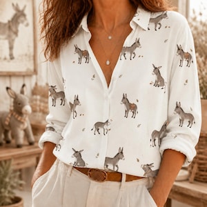 May include: A white long-sleeve button-down shirt featuring a repeating pattern of small grey donkeys. The shirt has a classic collar, a front button placket, and is worn tucked into light-colored trousers with a brown leather belt.