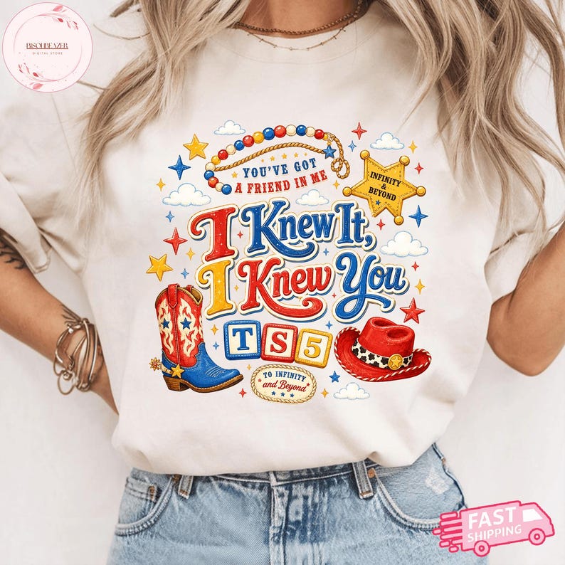 May include: A cream-colored t-shirt featuring a graphic print with a red and blue cowboy boot, a red cowboy hat, a yellow sheriff star, and colorful beads. The text reads: You've got a friend in me, I Knew It, I Knew You, TS5, and To Infinity and Beyond.