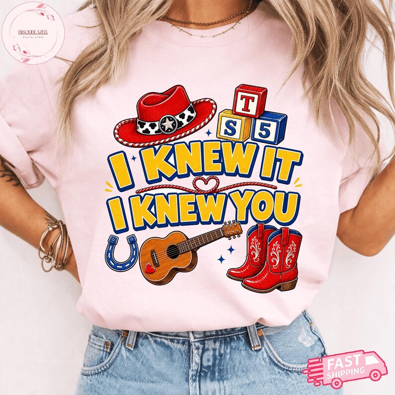 May include: A light pink t-shirt featuring a graphic print with a red cowboy hat, alphabet blocks labelled T, S, and 5, a brown acoustic guitar, and red cowboy boots. The text reads I KNEW IT I KNEW YOU in yellow letters with blue outlines.