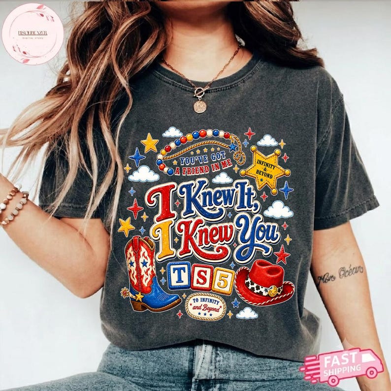 May include: A charcoal gray t-shirt featuring a graphic print with the text "I Knew It, I Knew You", "You've Got A Friend In Me", "Infinity & Beyond", and "TS5". The design includes a cowboy boot, a red cowboy hat, stars, and clouds.