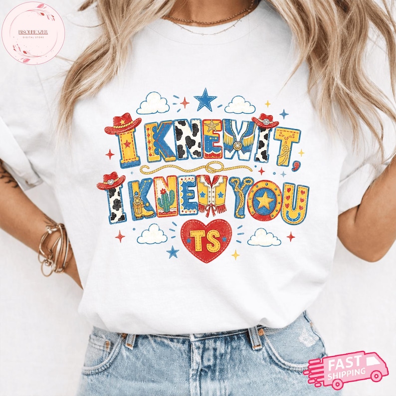 May include: A white t-shirt featuring a colorful graphic with the text I KNEW IT, I KNEW YOU and TS inside a red heart. The design includes cowboy hats, cow print patterns, stars, clouds, a cactus, and a lasso in shades of red, blue, and yellow.