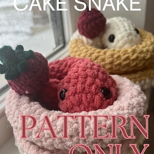 May include: Crocheted cake snakes in pink, yellow, and white, with a red cherry on top. The text "CAKE SNAKE" and "PATTERN ONLY" are visible. The snakes have black eyes and are nestled in a cupcake-like design.