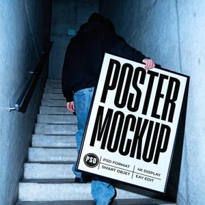 Puede incluir: Una persona lleva una maqueta de póster grande con las palabras "POSTER MOCKUP" en letras negras en negrita. El póster es blanco con un marco negro. La persona lleva una sudadera con capucha negra y vaqueros azules, subiendo una escalera de hormigón.