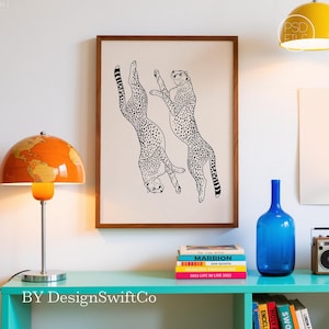 Puede incluir: Una impresión artística enmarcada con dos guepardos estilizados en blanco y negro. La obra de arte se muestra sobre un fondo claro dentro de un marco de madera marrón. La impresión se exhibe encima de una estantería turquesa con libros y una botella azul.