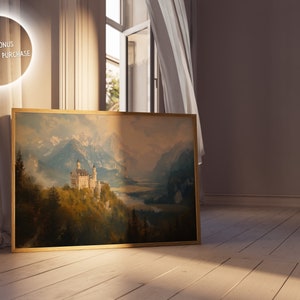 Op de afbeelding: Een ingelijst schilderij van een wit kasteel, genesteld in een bergketen met een meer op de voorgrond. Het schilderij is in een gouden lijst en hangt aan een muur.