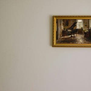May include: A framed painting of a grand piano in a room with a window and a few pieces of furniture. The painting is in a gold frame with ornate details.