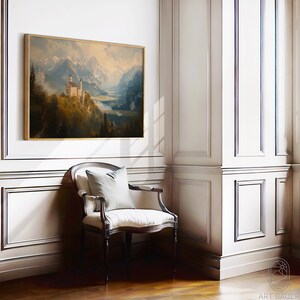 Op de afbeelding: Een ingelijst schilderij van een wit kasteel dat in een bergketen ligt met een meer op de voorgrond. Het schilderij hangt aan een witte muur in een kamer met een stoel en houten vloer.