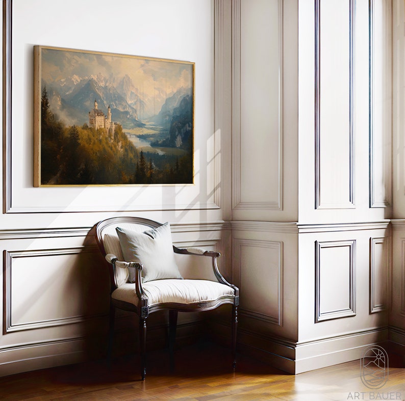 Op de afbeelding: Een ingelijst schilderij van een wit kasteel dat in een bergketen ligt met een meer op de voorgrond. Het schilderij hangt aan een witte muur in een kamer met een stoel en houten vloer.