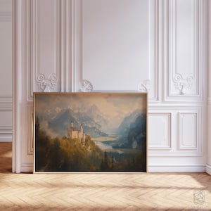 Op de afbeelding: Een ingelijste print van een schilderij dat een wit kasteel toont dat is genesteld in een bergketen met een rivier die door de vallei stroomt. De lucht is zachtblauw met wolken en de bergen zijn in gedempte groene en bruine tinten.