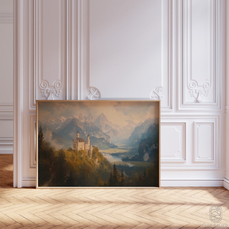 Op de afbeelding: Een ingelijste print van een schilderij dat een wit kasteel toont dat is genesteld in een bergketen met een rivier die door de vallei stroomt. De lucht is zachtblauw met wolken en de bergen zijn in gedempte groene en bruine tinten.