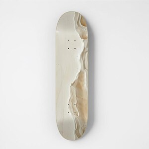 May include: A skateboard deck featuring a smooth, light cream-colored surface on the left side, transitioning into a textured, wavy pattern of beige and tan tones on the right side. The deck includes eight pre-drilled mounting holes.