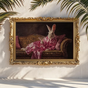 Könnte beinhalten: Ein gerahmtes Kunstwerk mit einem Kaninchen in einem rosa Bademantel, das einen Cocktail hält und auf einem Sofa mit Leopardenmuster liegt. Der verzierte goldene Rahmen verleiht diesem skurrilen Stück einen Hauch von Luxus. Palmenblätter umrahmen das Kunstwerk.